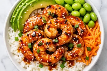shrimp rice bowl with garlic butter shrimp avocado edamame carrots and sesame seeds overhead flat lay